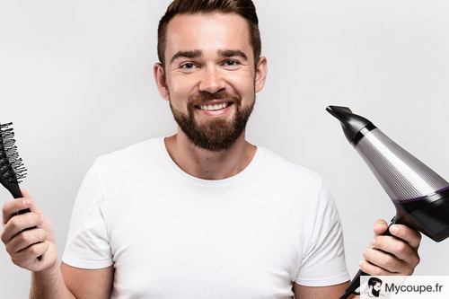 homme qui tient son sèche-cheveux ionique dans une main et une brosse dans l'autre main